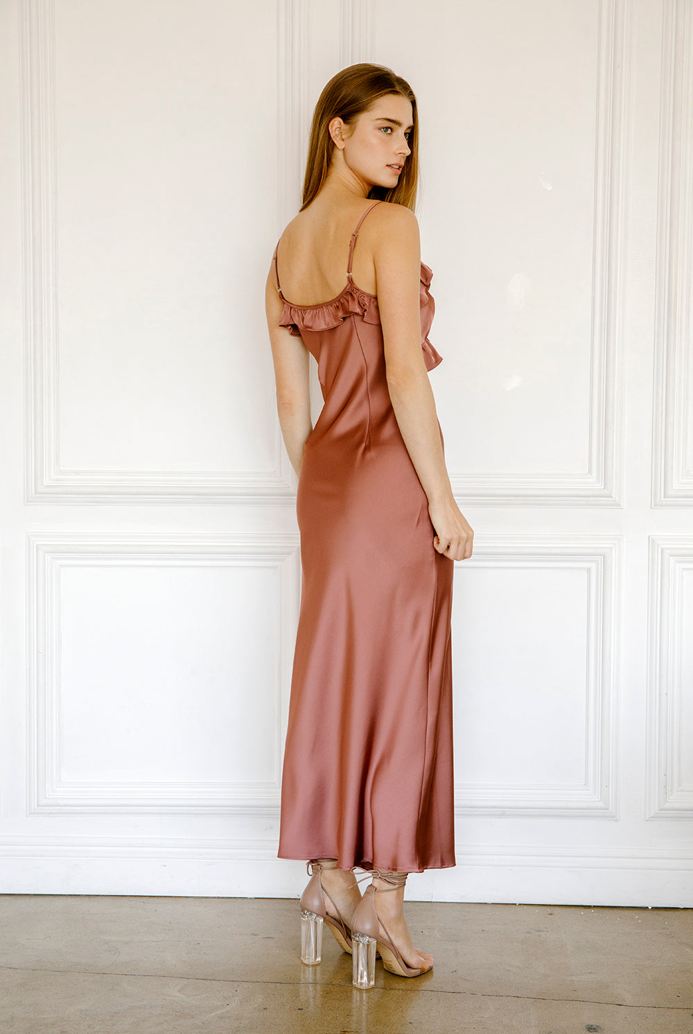 Back view of a woman wearing a mauve satin dress against a white paneled wall.