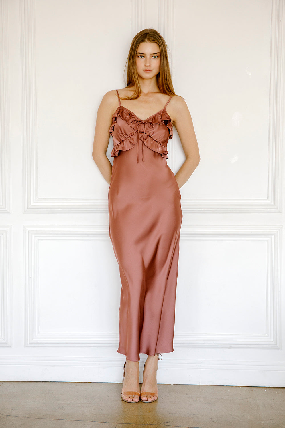 Woman wearing a mauve satin dress against a white paneled wall.