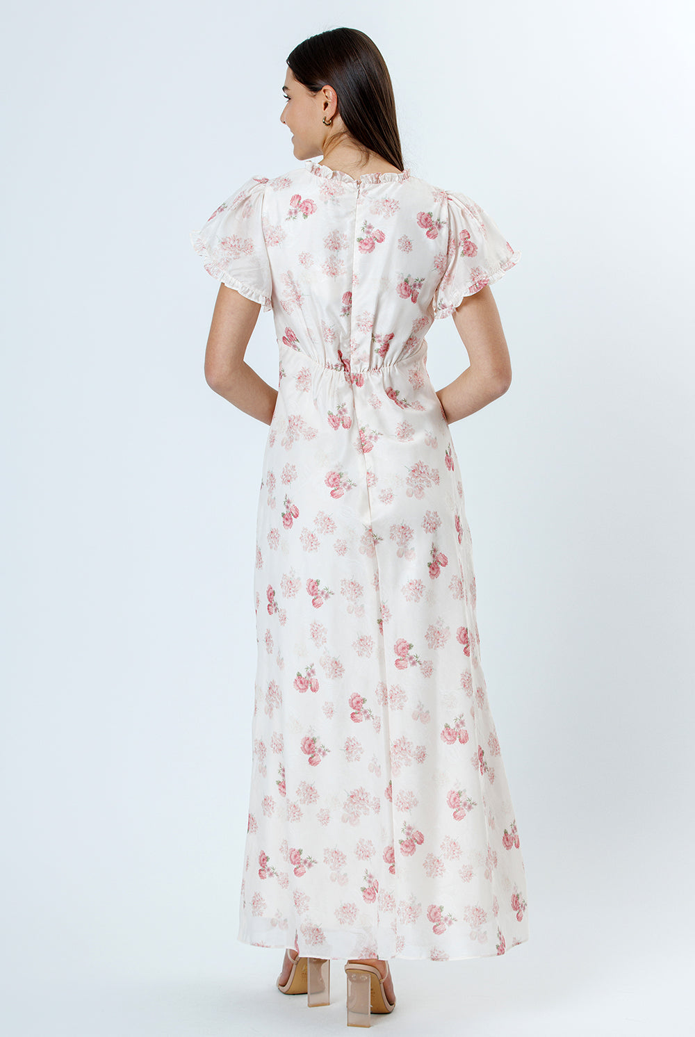 Back view of woman wearing a pink and white floral dress with flutter sleeves on a white background