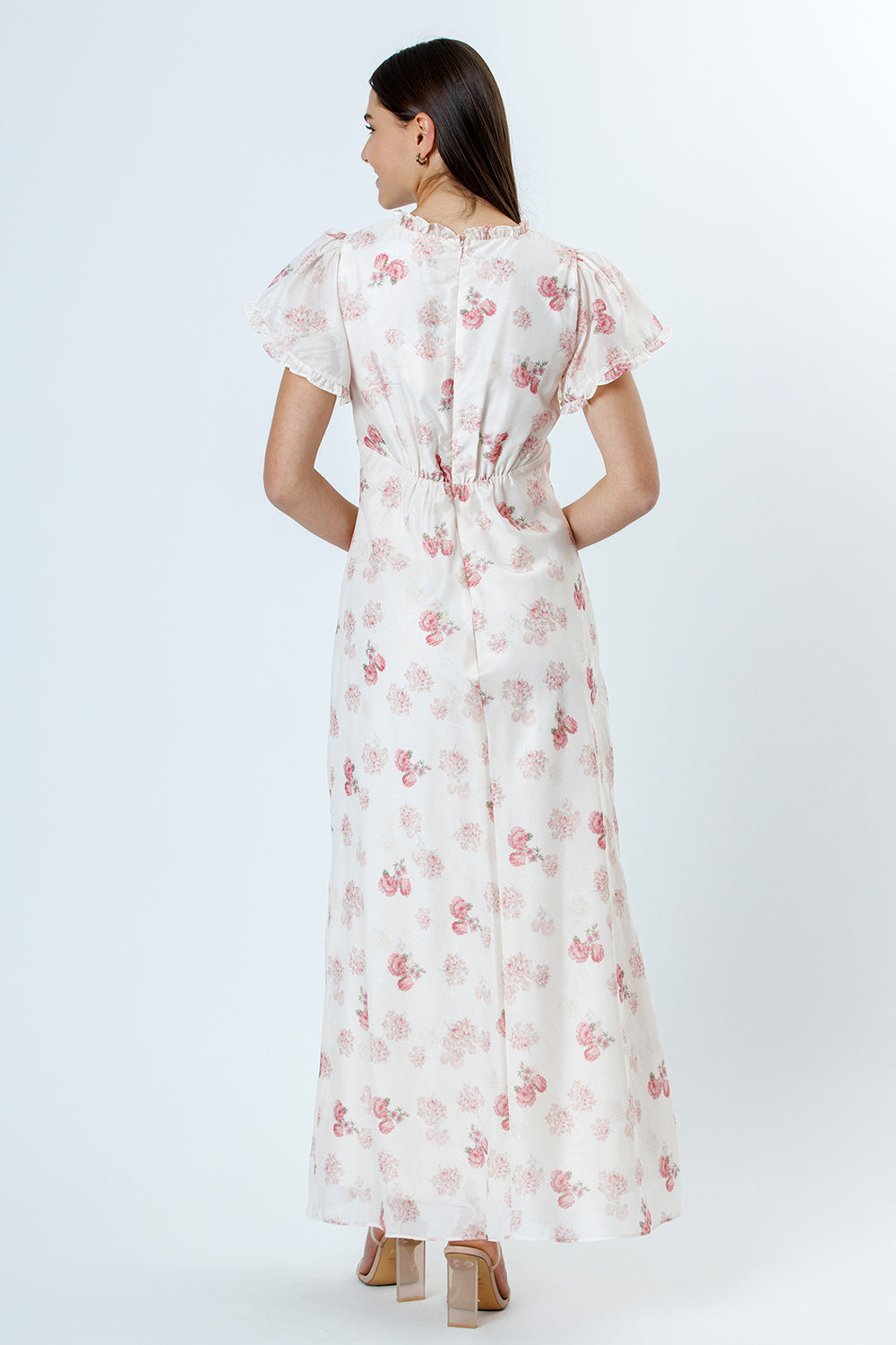 Back view of woman wearing a pink and white floral dress with flutter sleeves on a white background