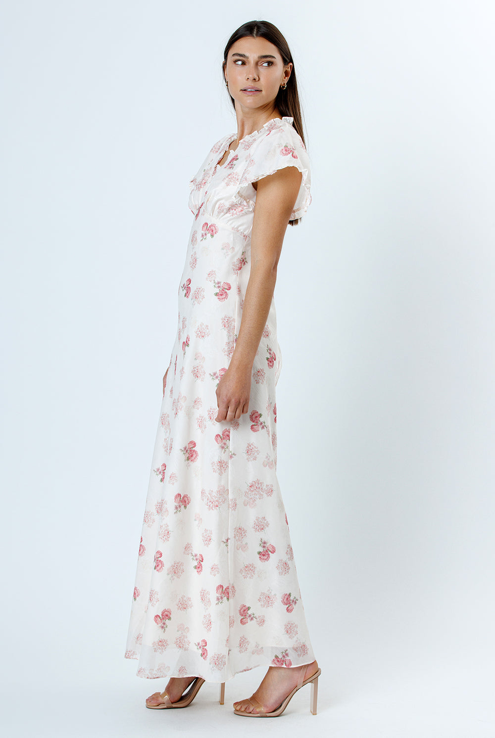 Side view of a woman wearing a pink and white floral dress with flutter sleeves on a white background