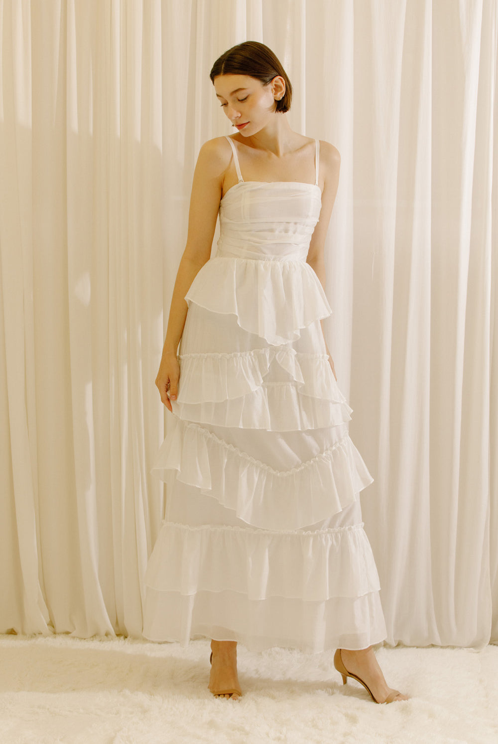 Woman wearing a white tiered maxi dress against a plain background
