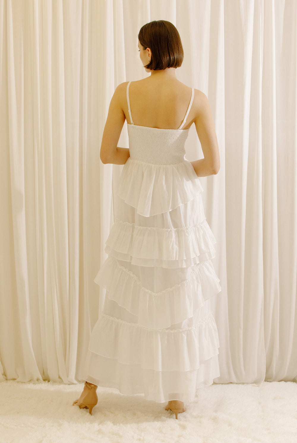 Back view of a woman wearing a white maxi dress standing in front of sheer curtains