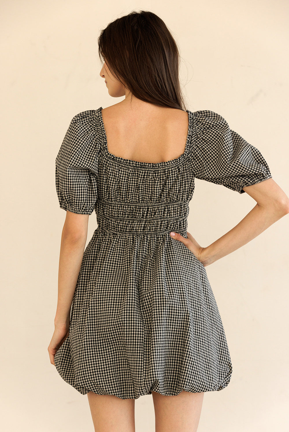 Woman wearing a checkered dress with puff sleeves on a beige background