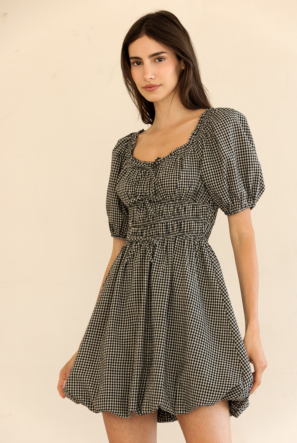 Woman wearing a black and beige checkered dress against a beige background