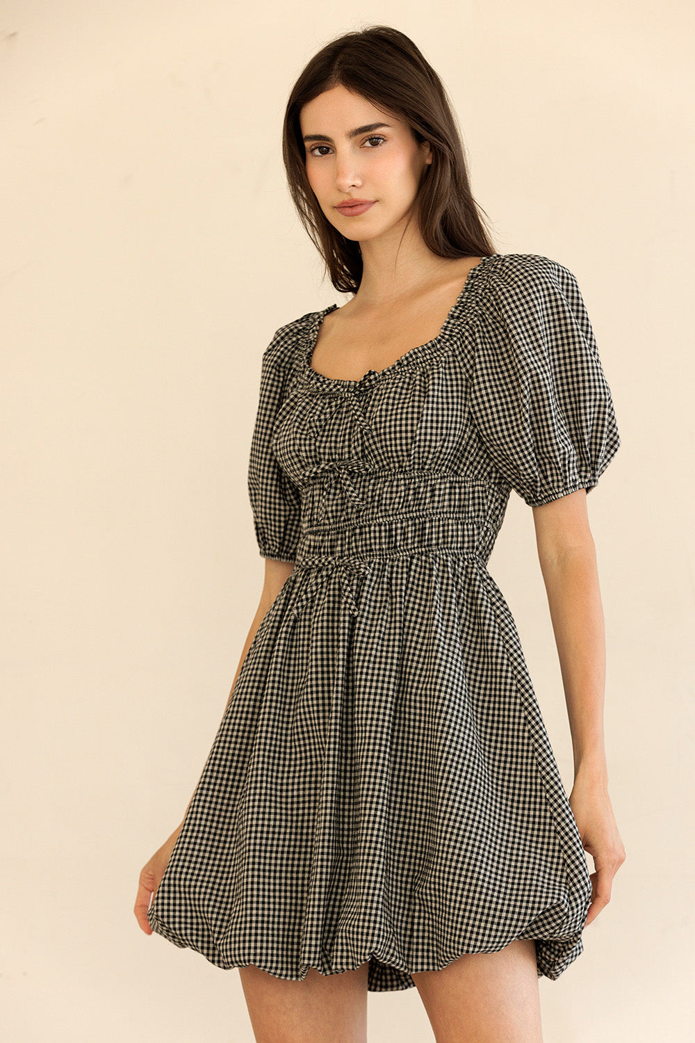 Woman wearing a black and beige checkered dress against a beige background