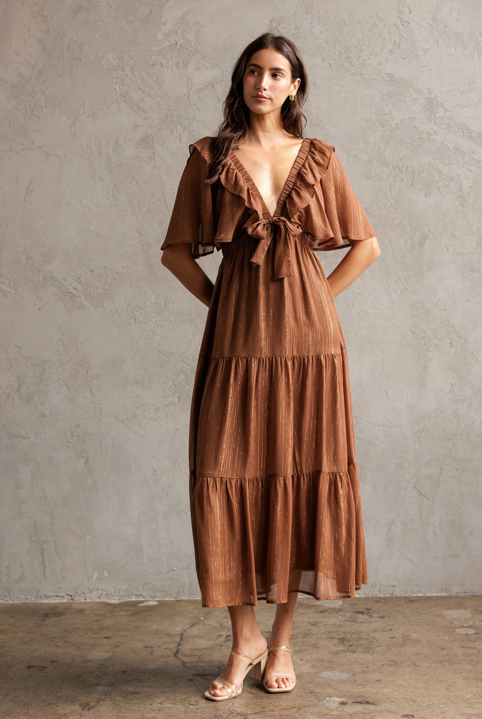 Woman wearing a brown dress against a gray concrete wall