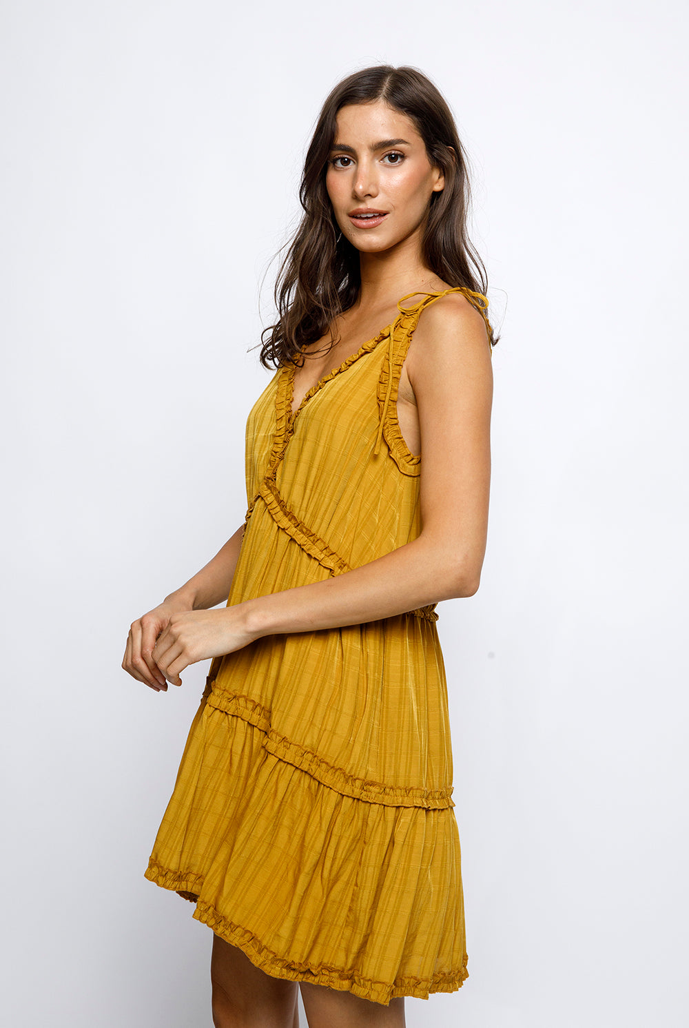 Side view of a woman wearing a mustard yellow dress against a white background