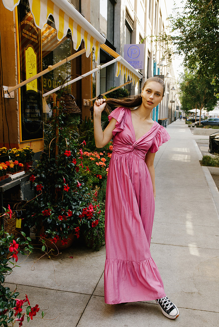 Woman in a pink maxi dress and black sneakers standing in front of a flower store