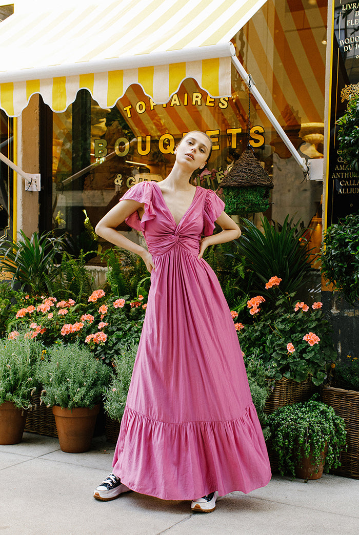 Woman in a pink maxi dress standing in front of a store with a striped awning.