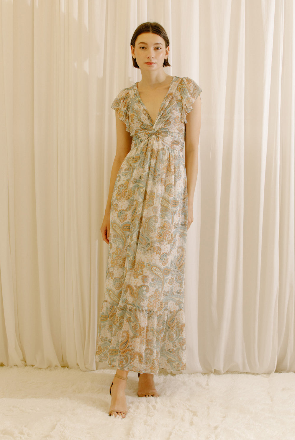 Woman wearing a beige floral dress standing against a plain background