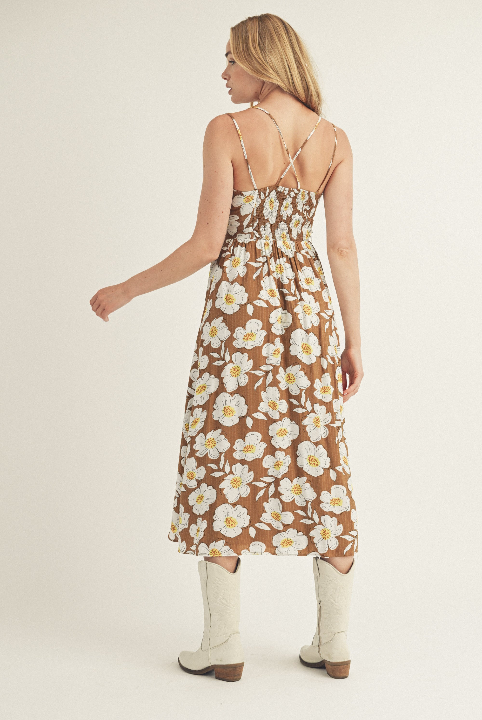 Back view of a woman wearing a brown and white floral dress and white boots on a plain background