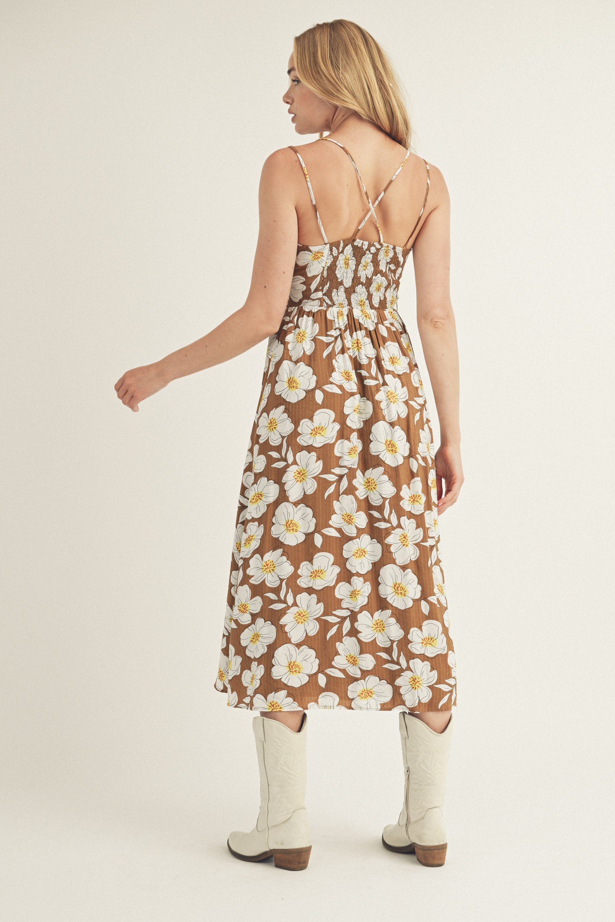 Back view of a woman wearing a brown and white floral dress and white boots on a plain background