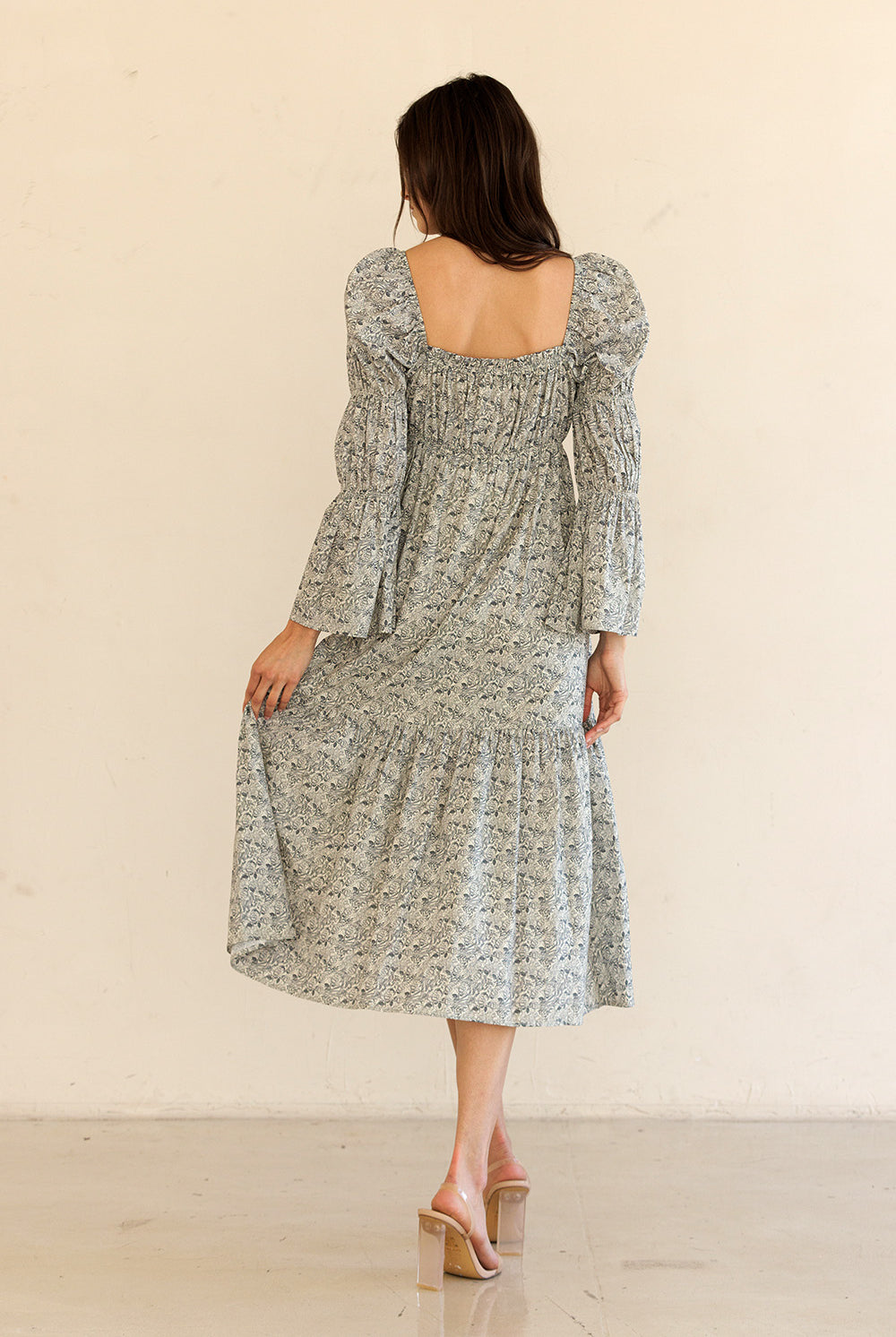 Back view of a woman wearing a navy floral dress with long sleeves against a beige background