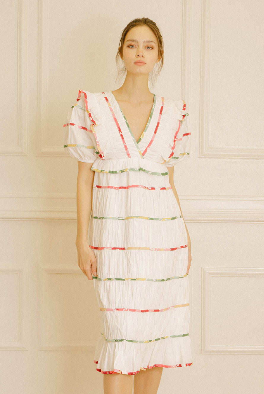 Woman wearing a white dress with colorful stripes against a beige wall.