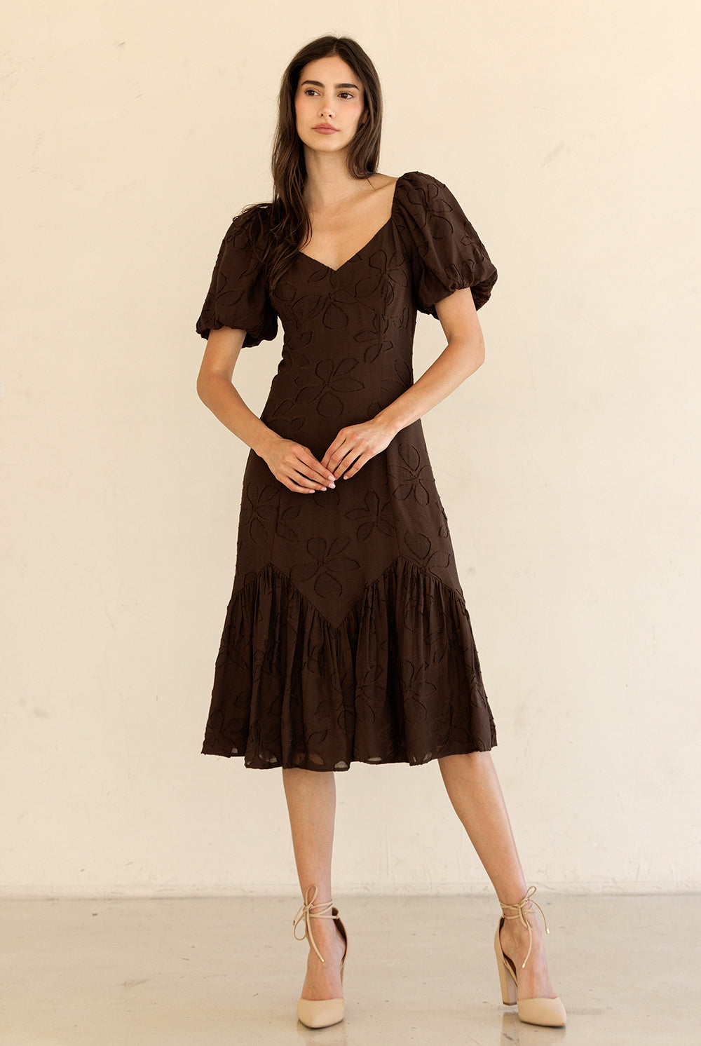 Woman wearing a brown dress with puff sleeves against a beige background