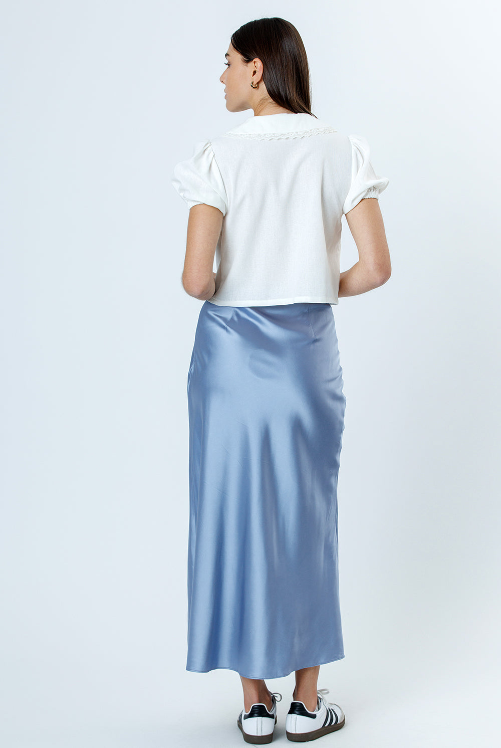 Back view of a woman wearing a white top and light blue satin skirt on a white background