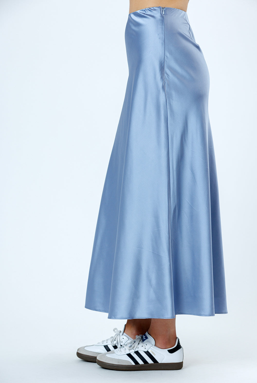 Side view of a light blue satin skirt worn with white Adidas sneakers on a white background