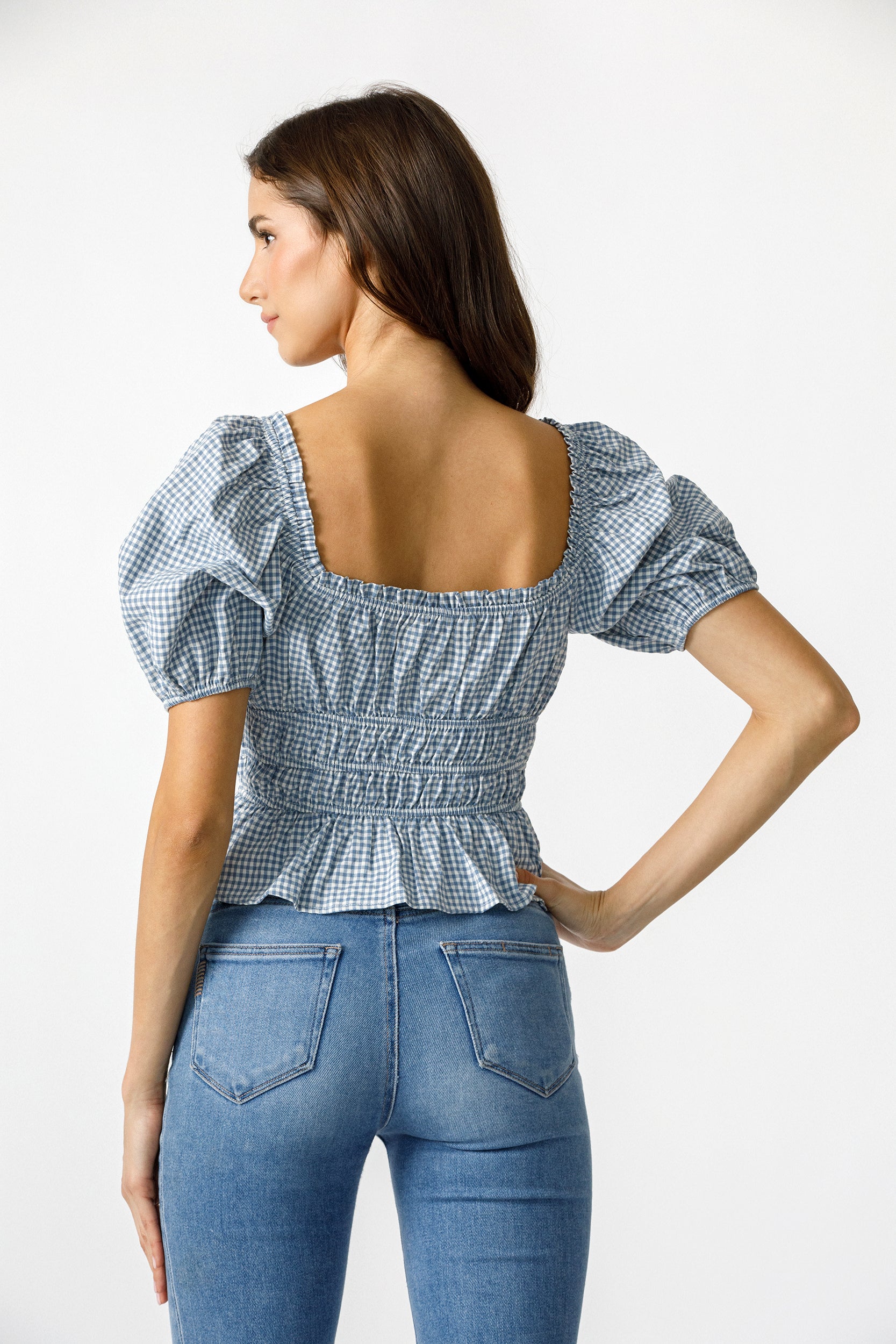 Back view of a woman wearing a blue checkered top and jeans on a white background