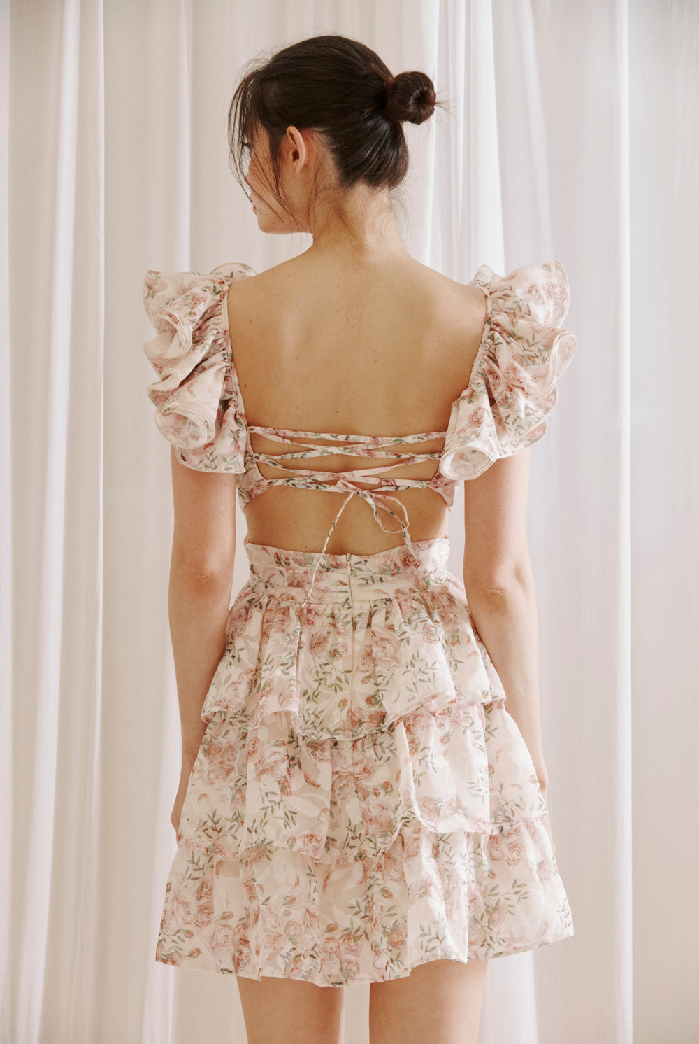Back view of blush floral ruffle mini dress with open back and lace-up tie