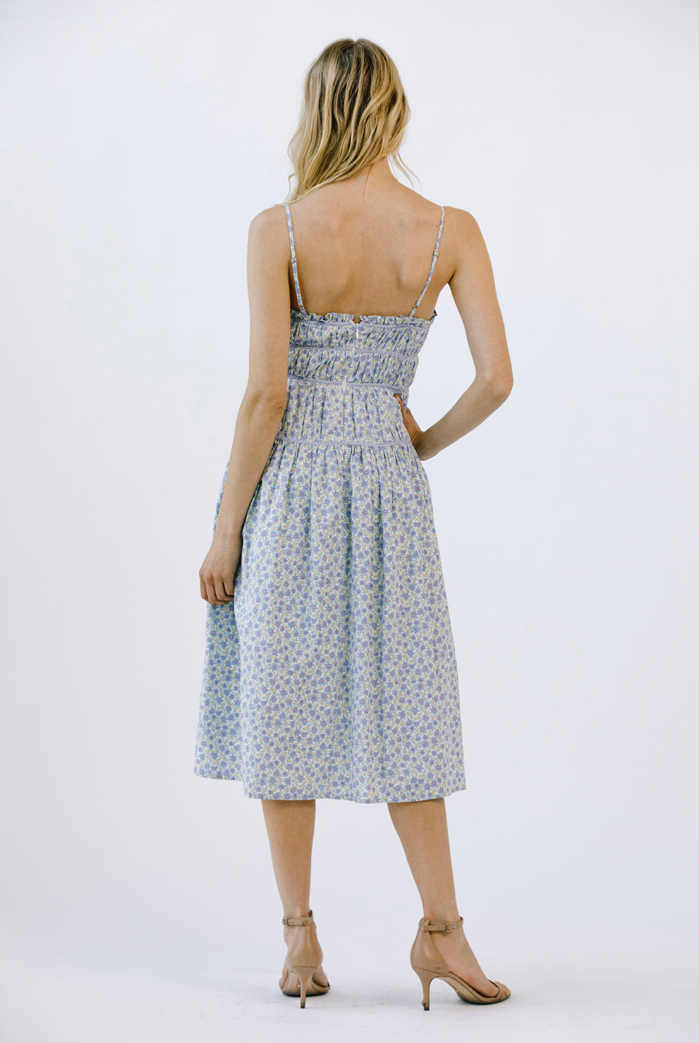 Back view of a woman wearing a blue floral midi dress on a white background
