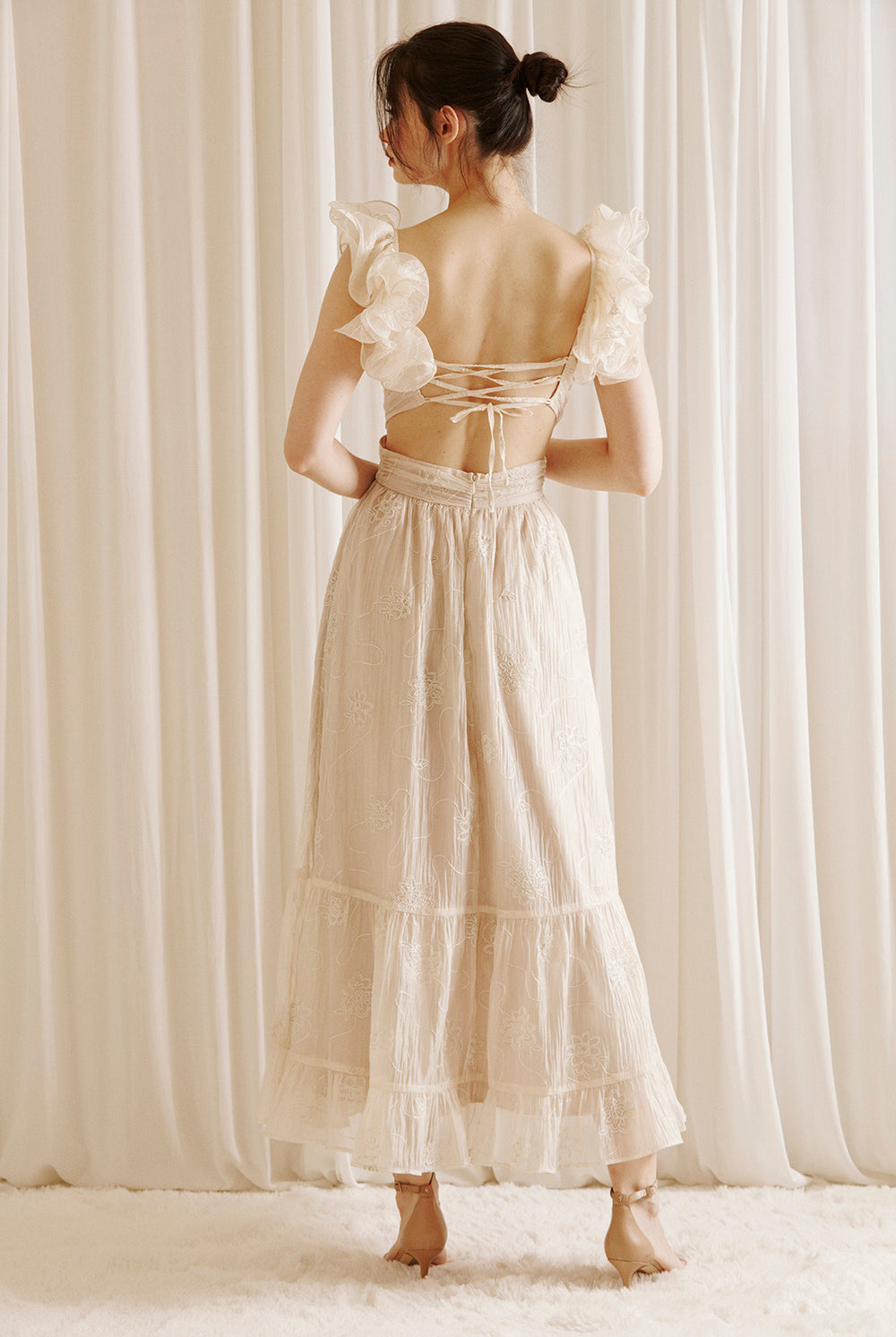 Back view of a woman wearing a beige maxi dress with embroidered flowers