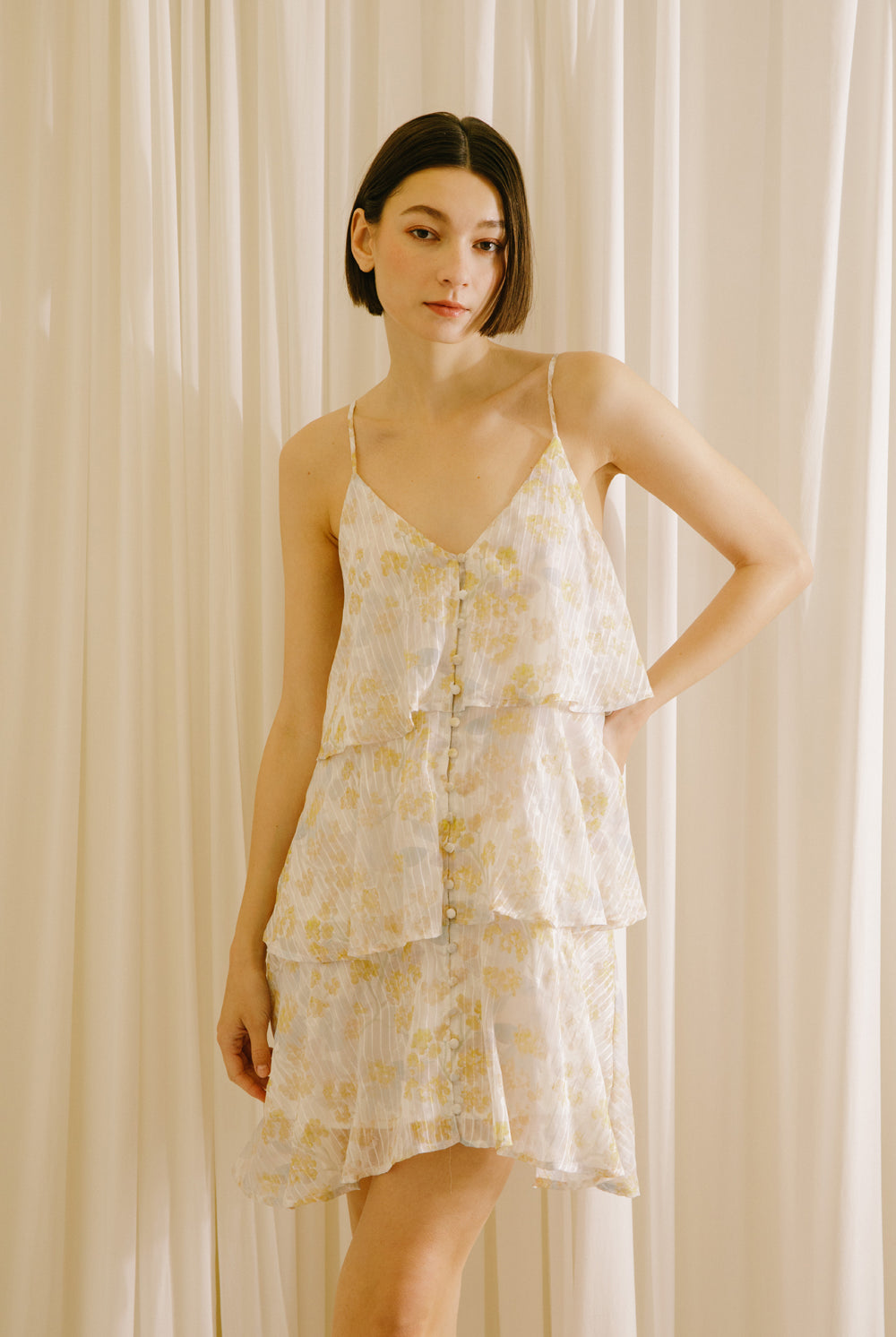 Woman wearing a yellow slip dress with floral and stripe pattern against a beige curtain background
