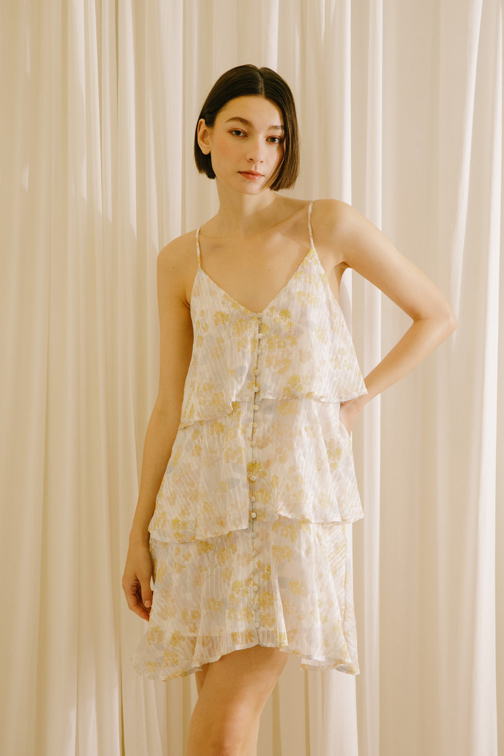 Woman wearing a yellow slip dress with floral and stripe pattern against a beige curtain background