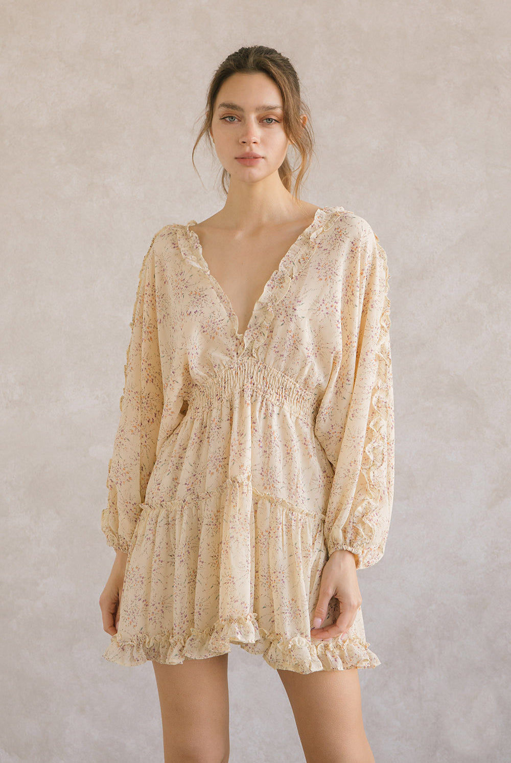 Woman wearing a yellow dress with long sleeves and a v-neckline with ruffle trimming against a plain background