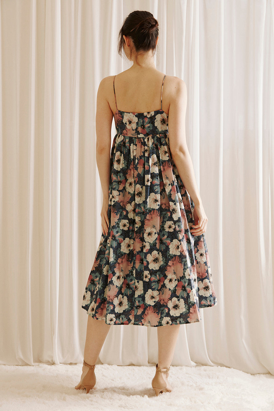 Back view of a woman wearing a navy floral midi dress standing against a white curtain background