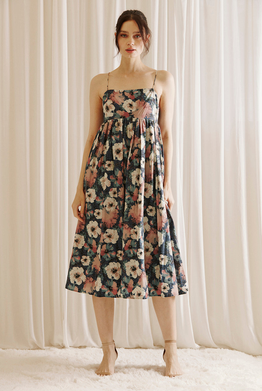 Woman wearing a navy floral midi dress standing against a white curtain background
