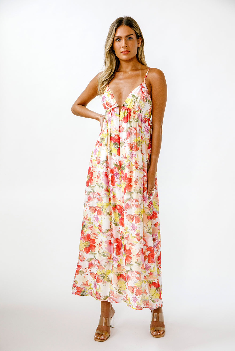 A woman modeling a sleeveless maxi dress with thin straps and a colorful floral print on a white background.