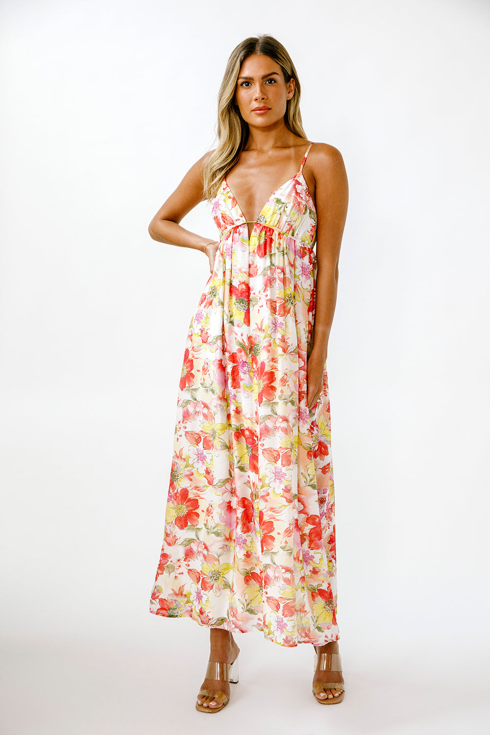 A woman modeling a sleeveless maxi dress with thin straps and a colorful floral print on a white background.