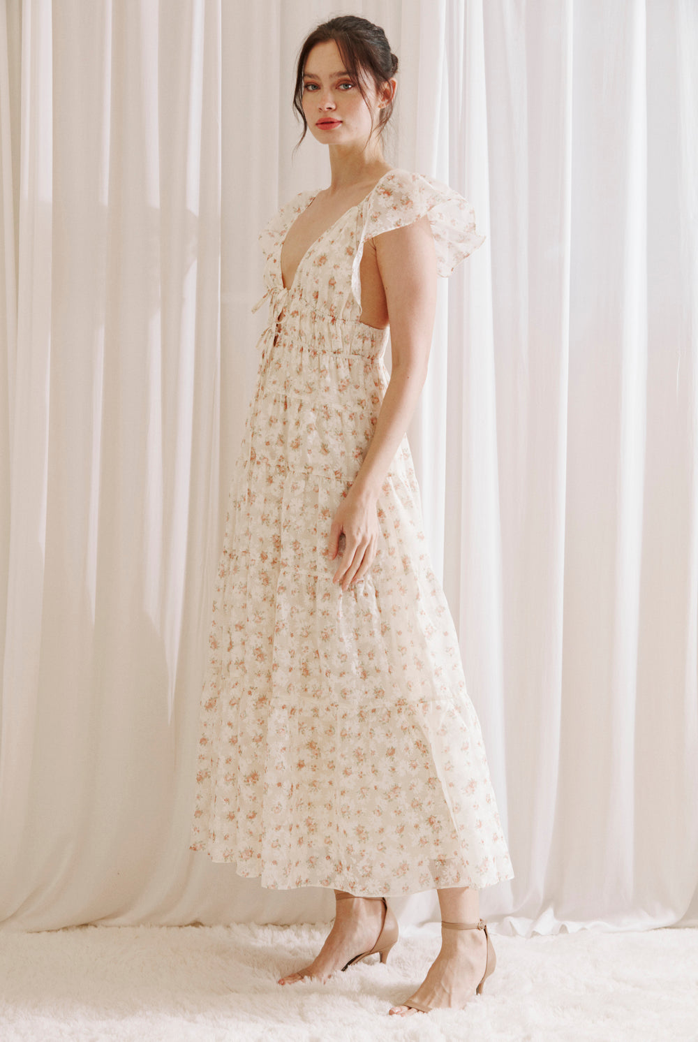 Side view of a woman wearing a floral dress against a white curtain background