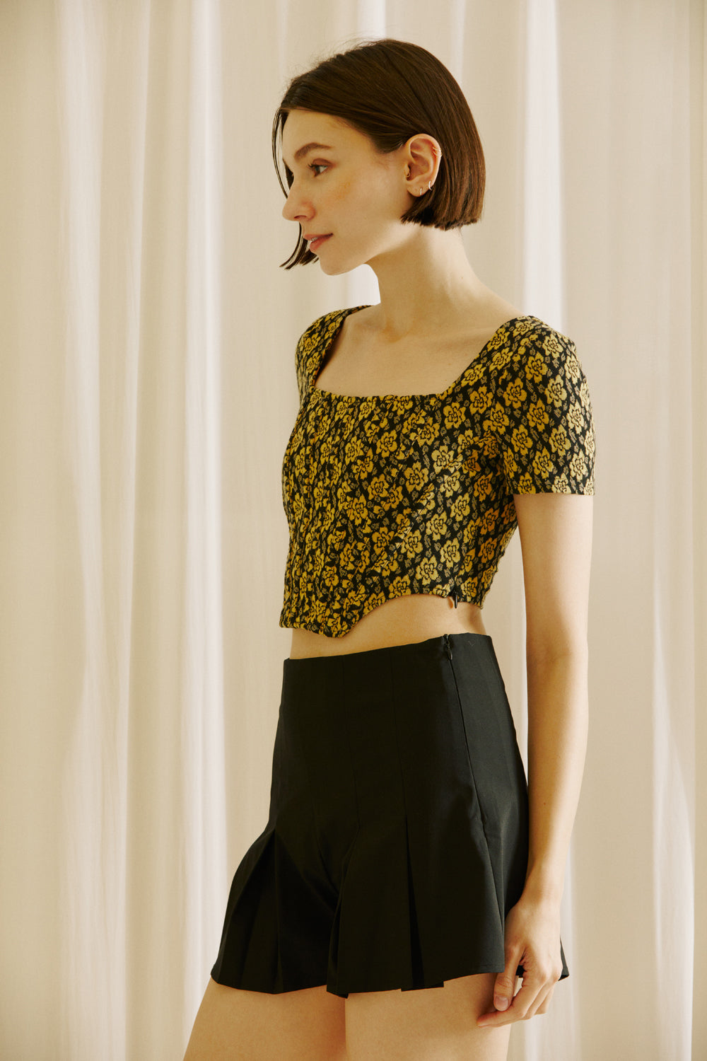 Side view of a woman wearing a floral top and black shorts against a beige curtain background