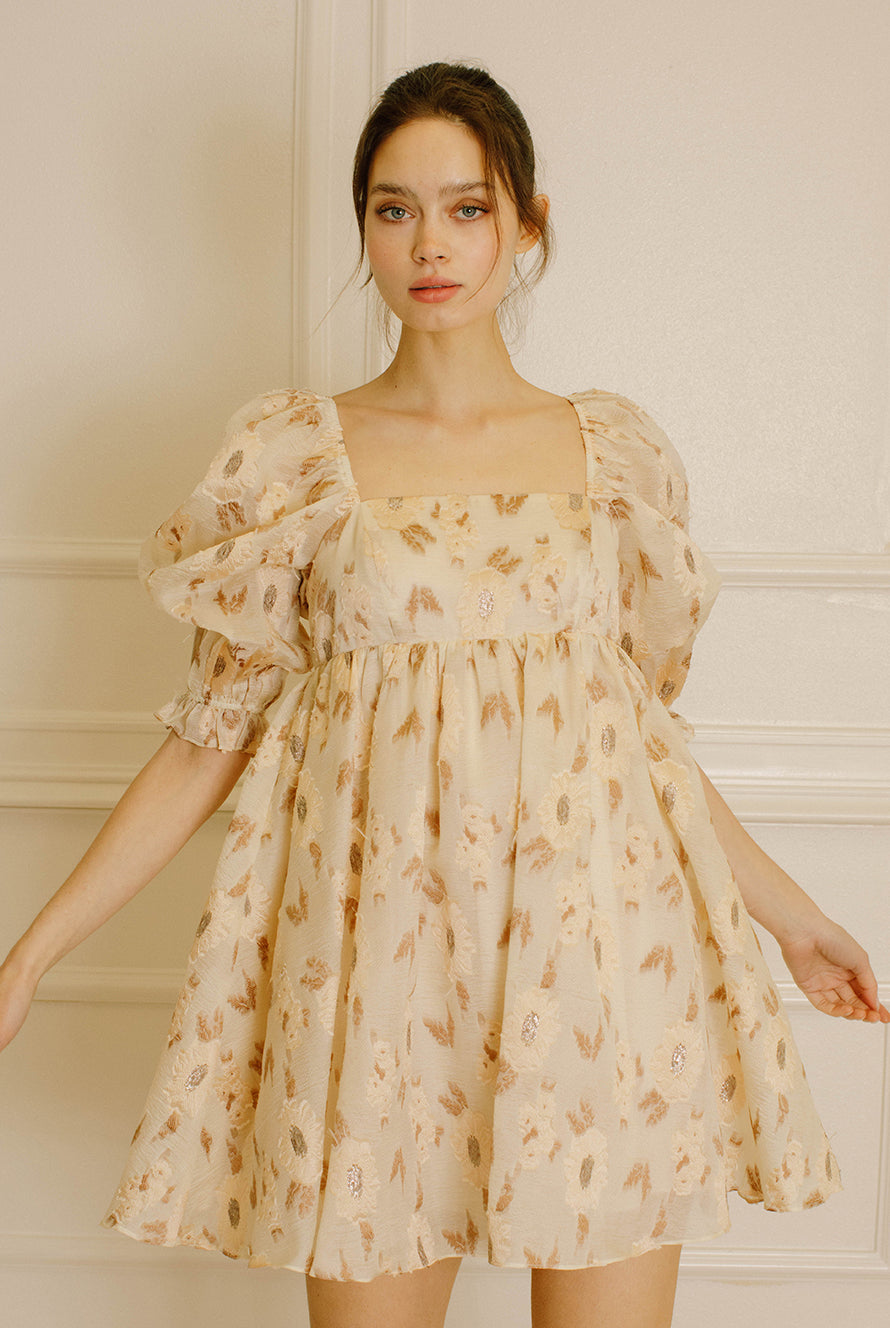Woman wearing a beige dress with a floral pattern in an indoor setting