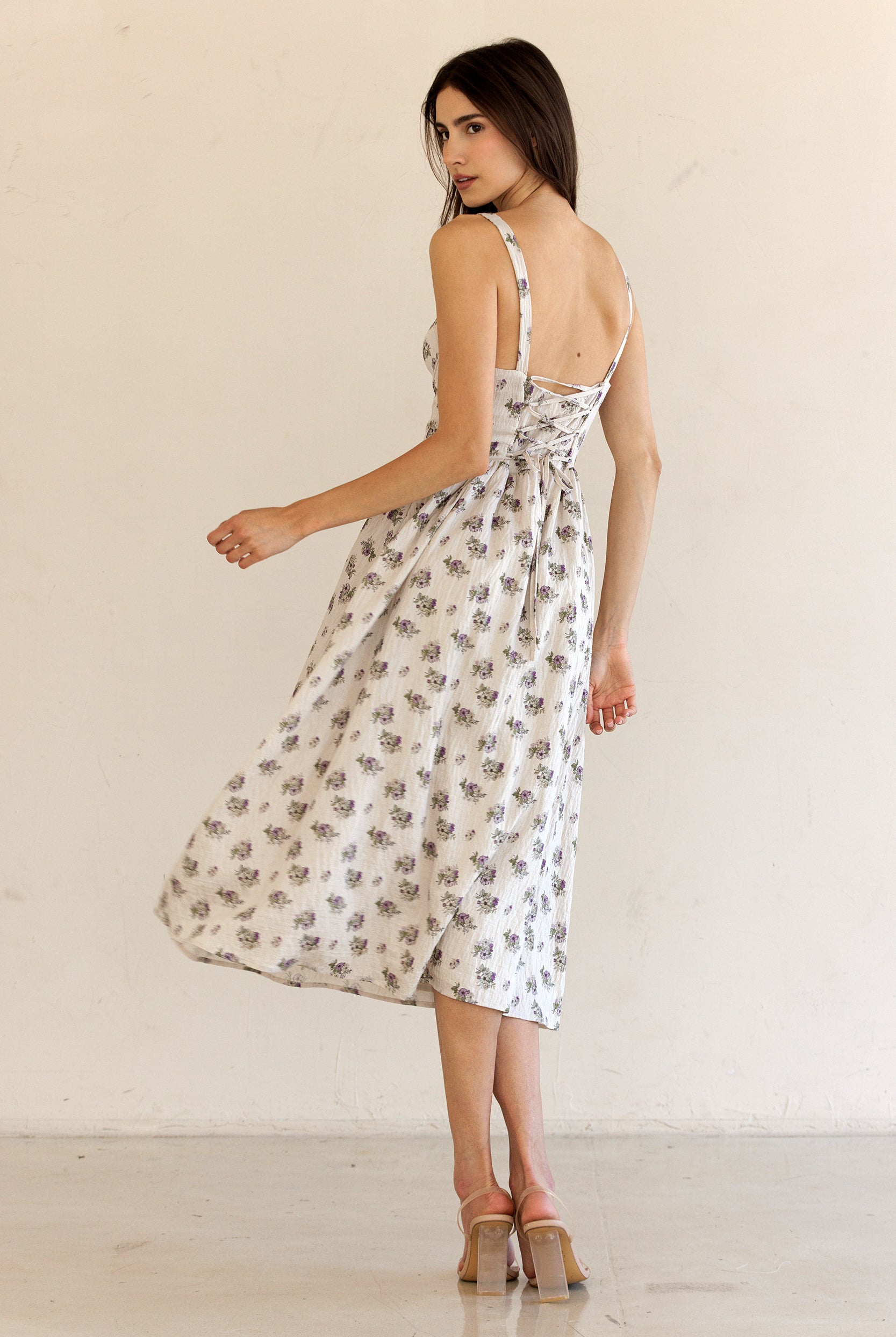 Back view of a woman wearing a beige floral dress against a plain background