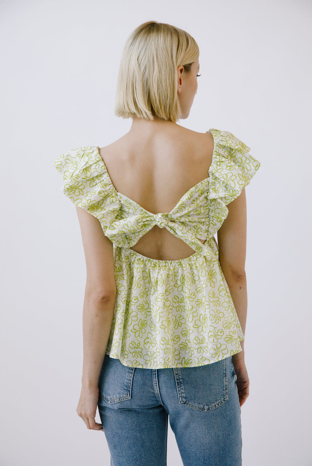 Woman wearing a light green floral top with a bow back design on a white background