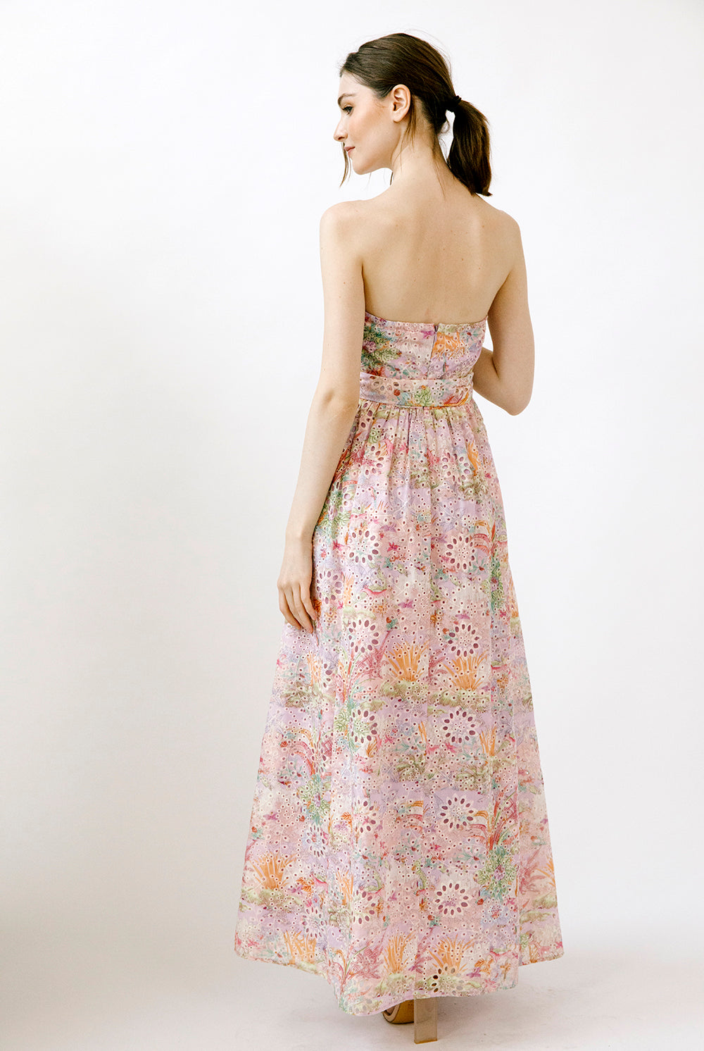 Back view of a woman wearing a colorful floral print strapless dress on a white background