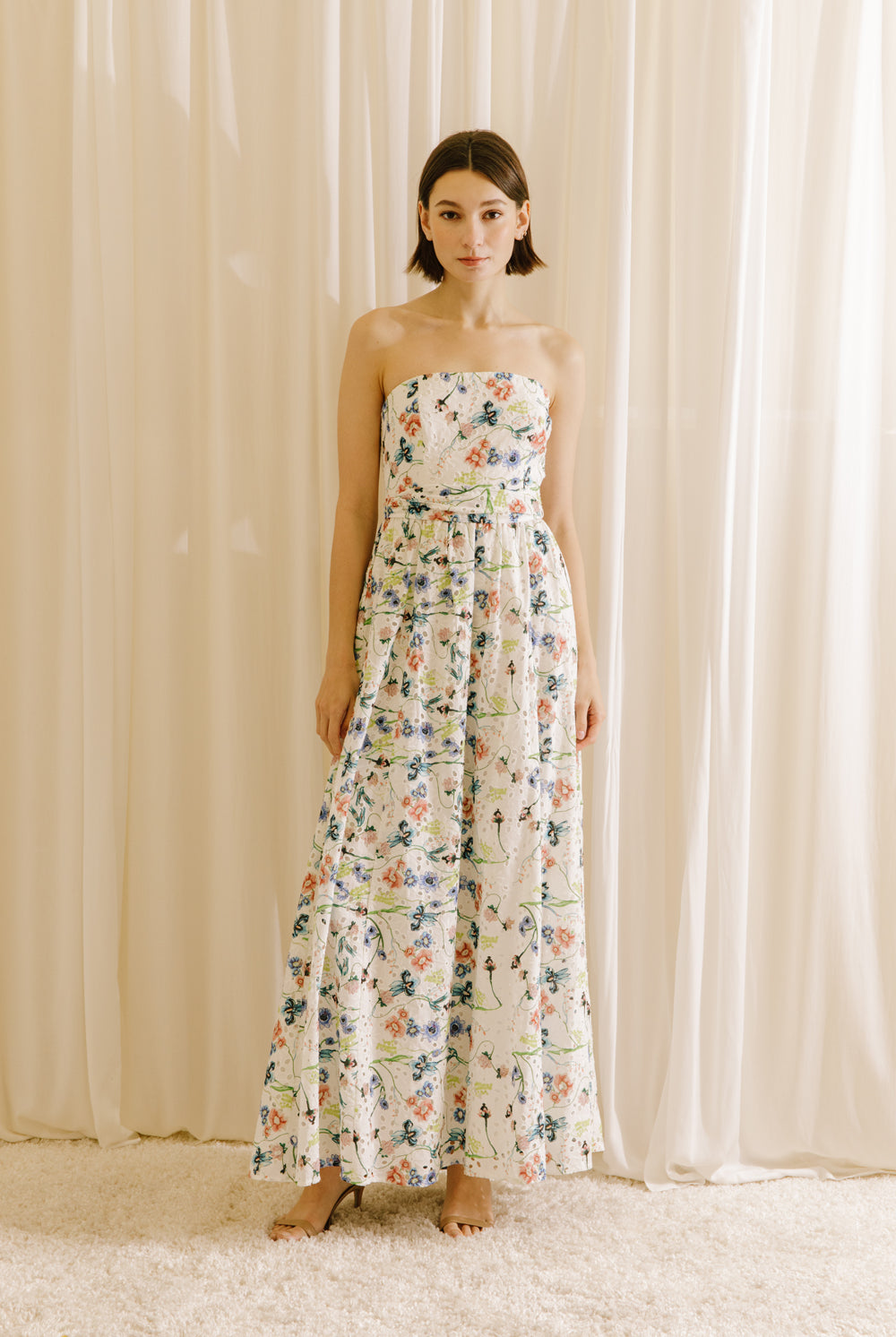Woman wearing a blue floral strapless dress against a beige curtain background