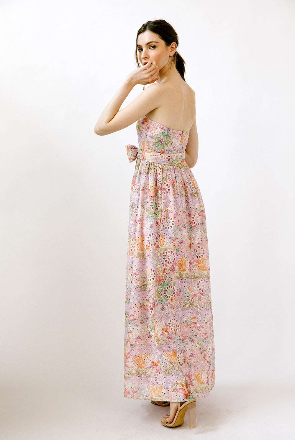 Side view of a woman wearing a colorful floral print on embroidered eyelet fabric dress on a white background