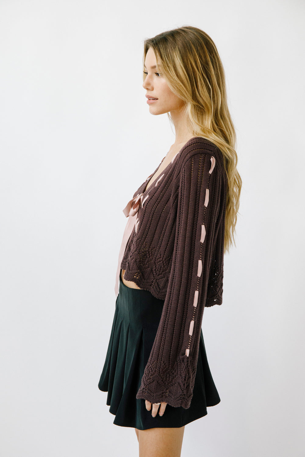 Side view of a woman wearing an eggplant cardigan and black skirt on a white background