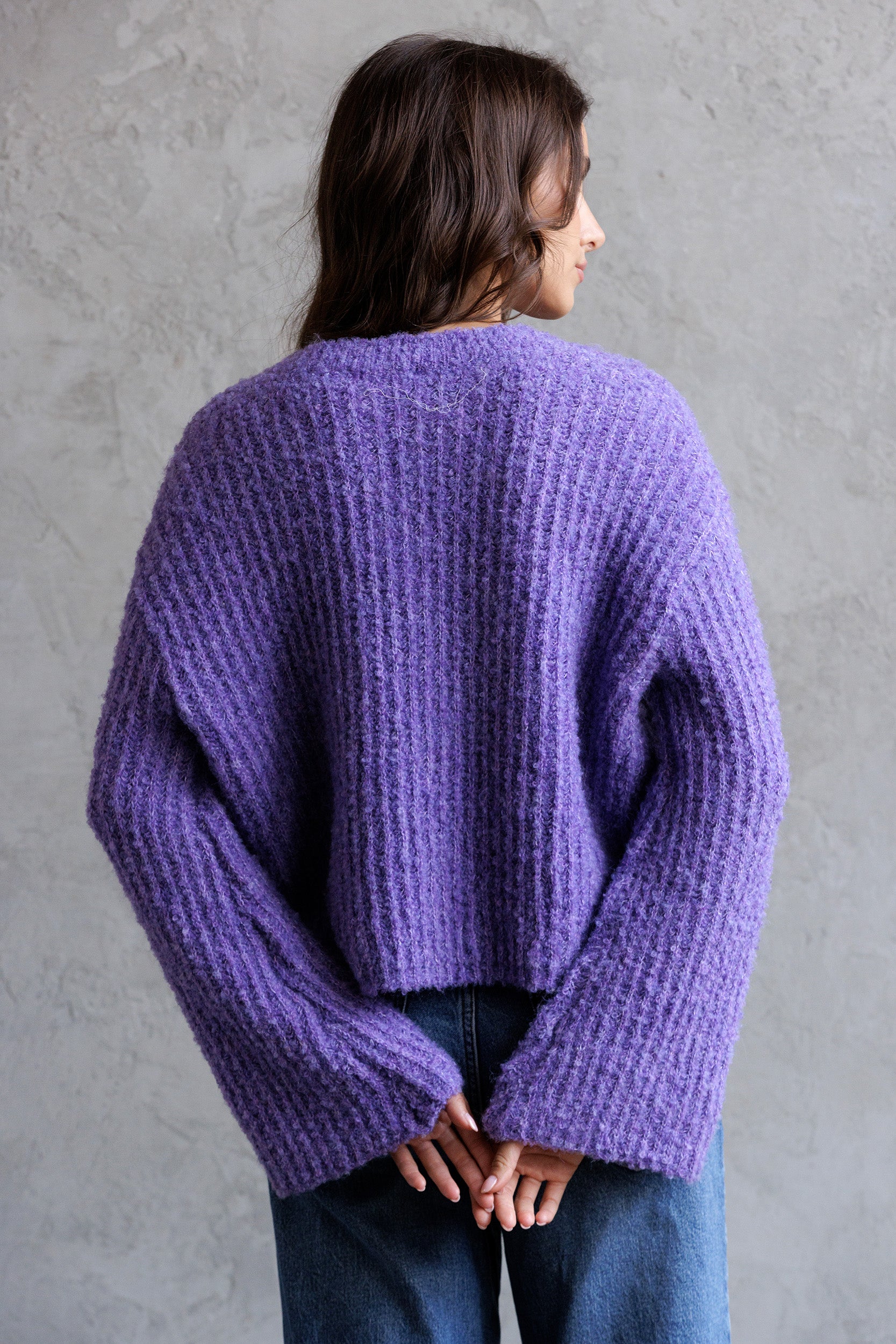 Back view of a model wearing a purple sweater against a gray background