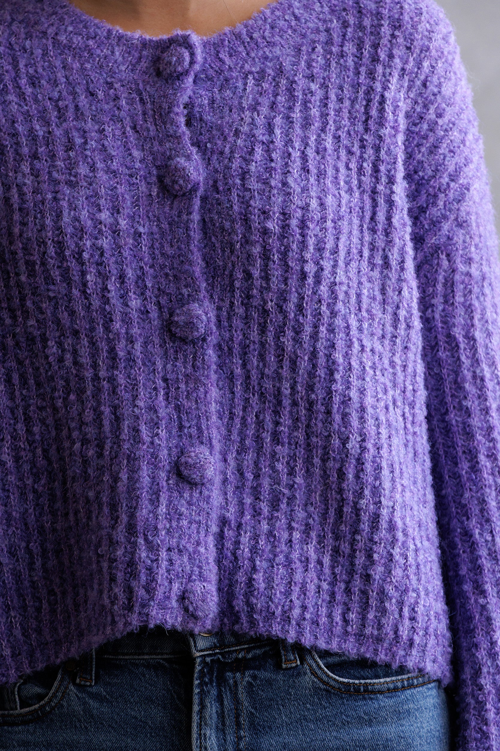Close-up of a purple knitted cardigan with buttons.