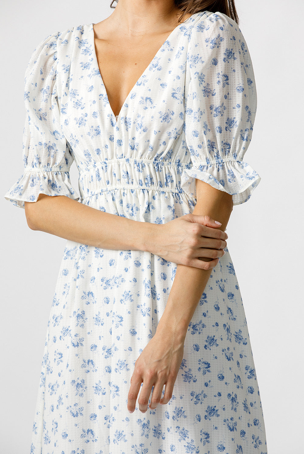 White dress with blue floral pattern worn by a person on a plain background