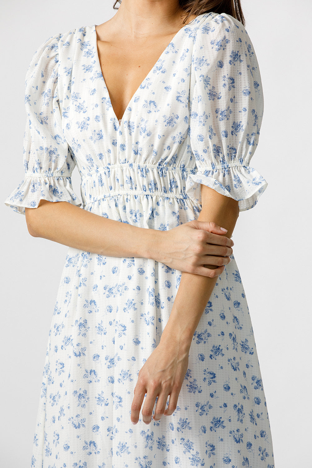 White dress with blue floral pattern worn by a person on a plain background