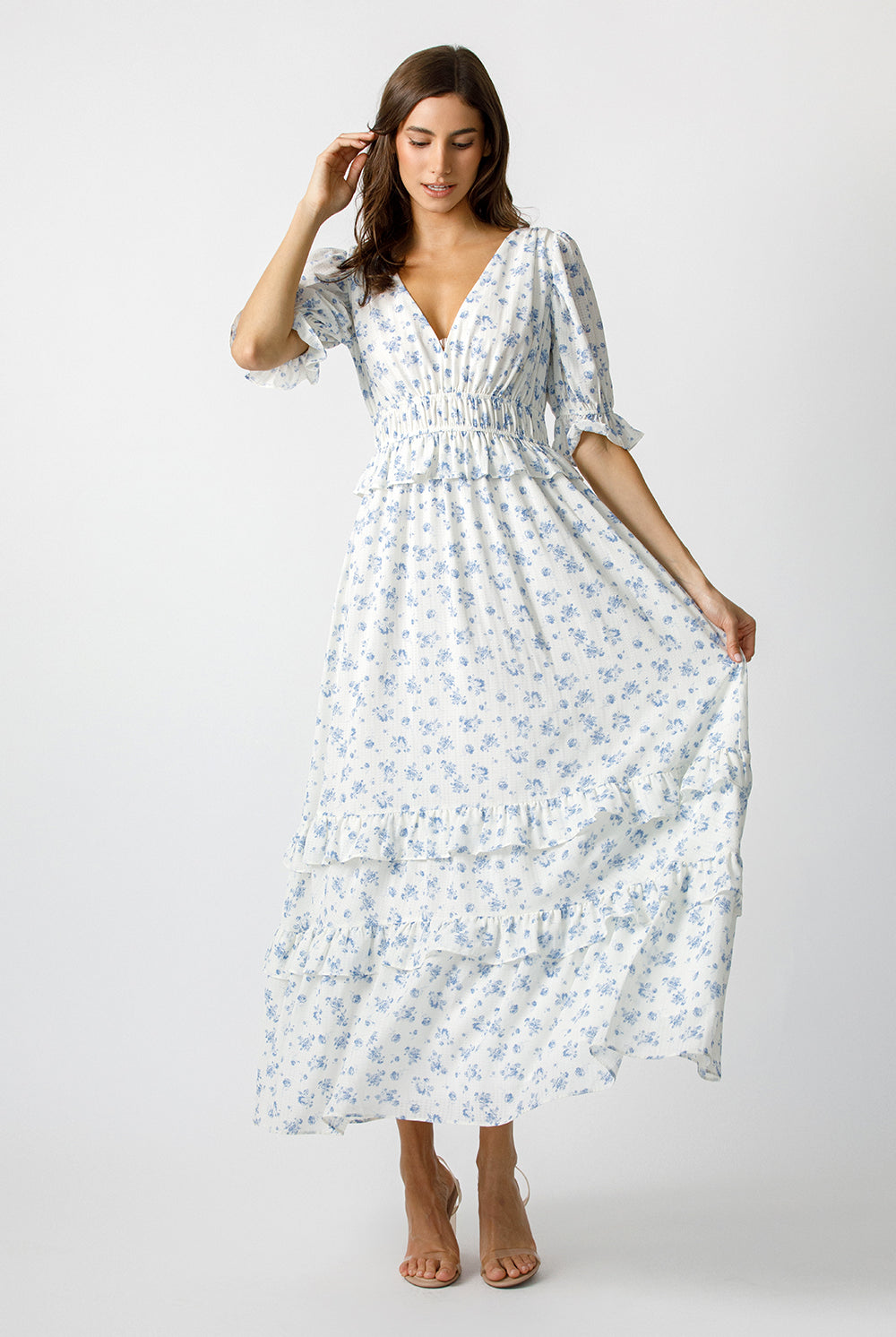 Woman wearing a blue and white floral dress and beige high-heels on a white background