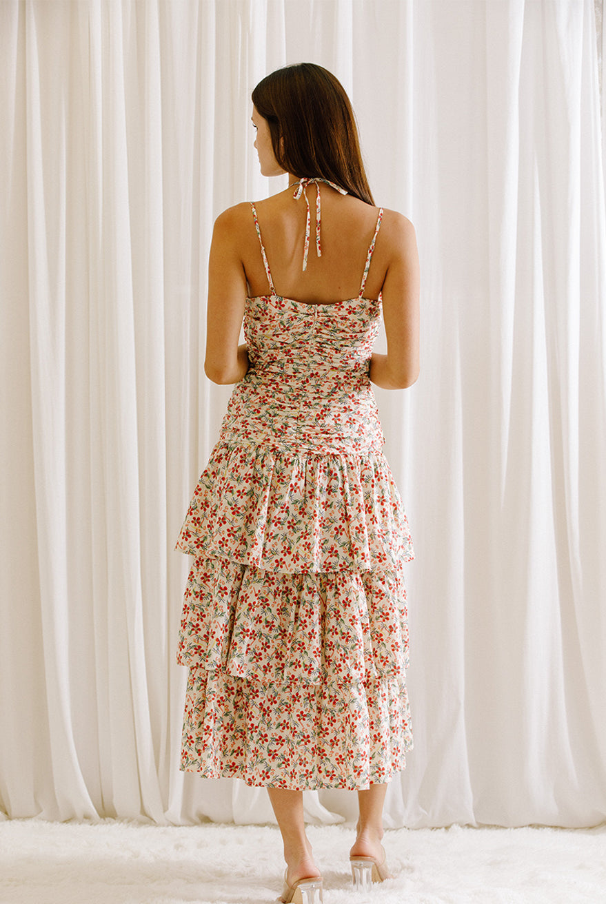 Back view of a woman wearing a floral dress with ruched upper body standing against a white curtain