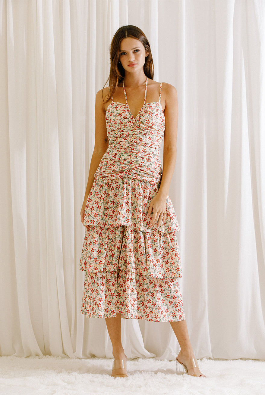 Woman wearing a floral dress with ruched upper body standing against a white curtain