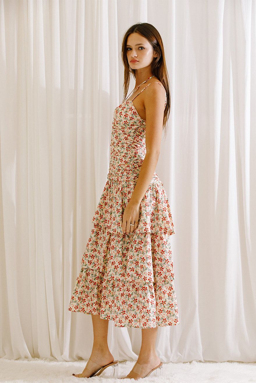 Side view of a woman wearing a floral midi dress with ruched upper body standing against a white curtain